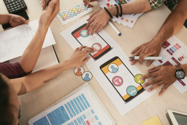 Manos diseñando interfaz de app móvil con íconos de juegos y música